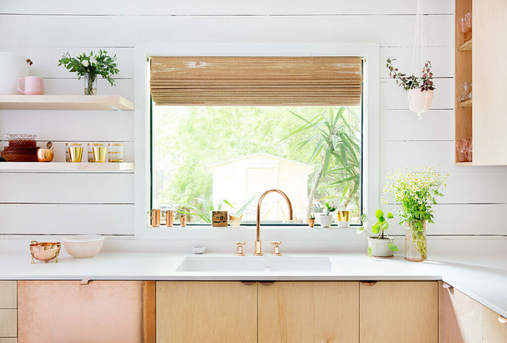 Bright kitchen featuring a white countertop, natural wood cabinets, and a cozy window view with plants.