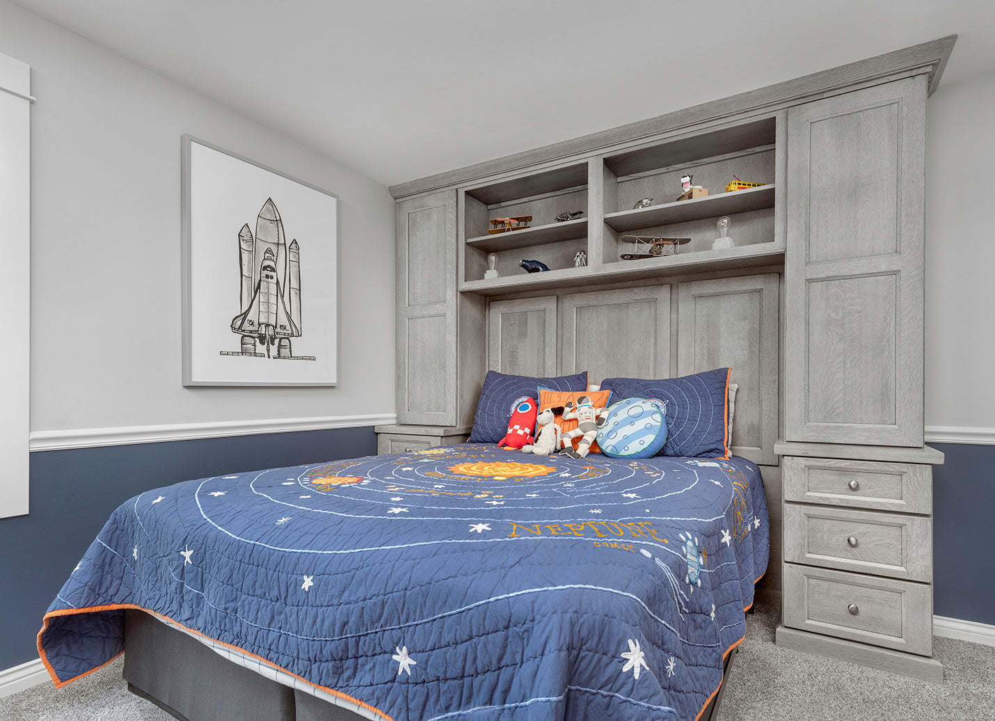 Modern boys' bedroom featuring gray cabinets, a star-themed quilt, plush toys, and space artwork.