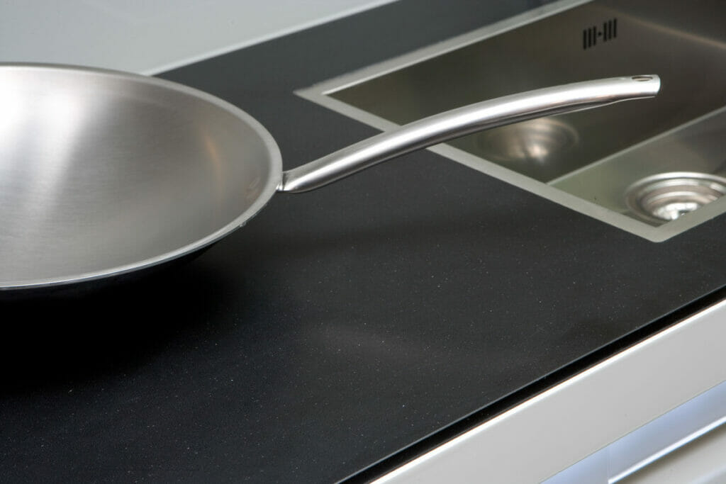 Stainless steel frying pan on sleek 3100 Jet Black countertop, showcasing luxury and sophistication in kitchen design.