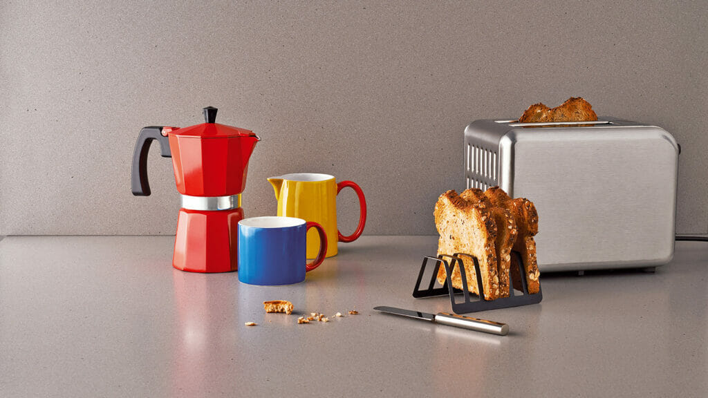Colorful kitchen scene with a red coffee maker, yellow and blue mugs, and toast in a modern silver toaster.