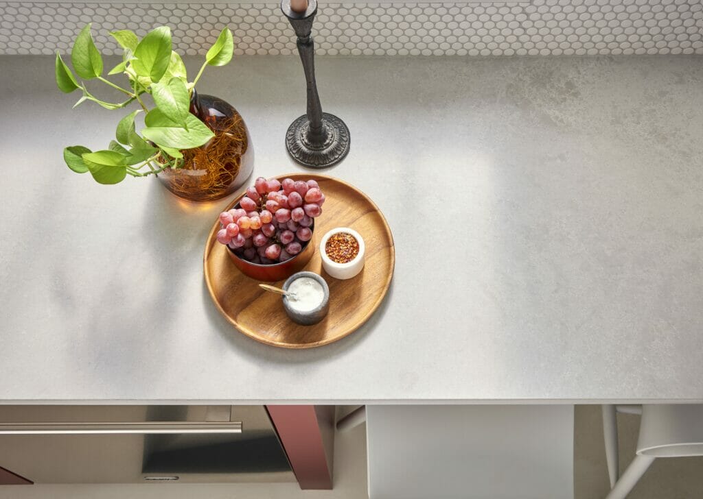Airy concrete countertop with a wooden tray, grapes, dip, and a potted plant on a textured surface.