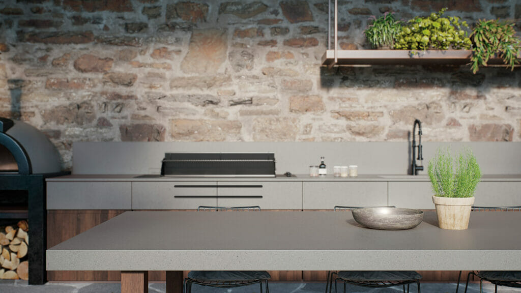 Modern kitchen featuring smooth concrete grey surfaces and stone wall, with plants and rustic oven in the background.