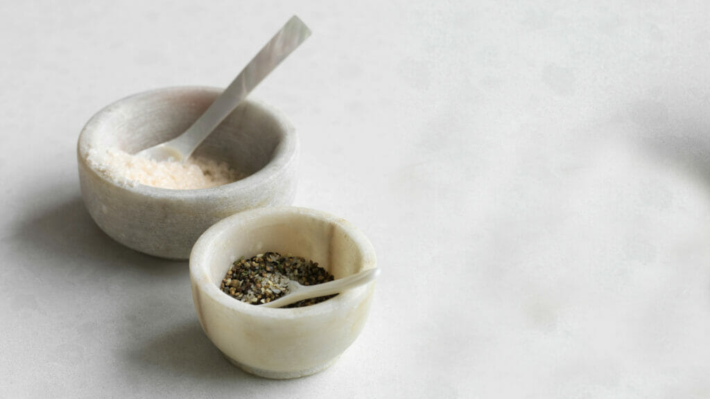 Two marble bowls with salt and pepper, featuring elegant spoons on a clean, light surface for a chic kitchen aesthetic.