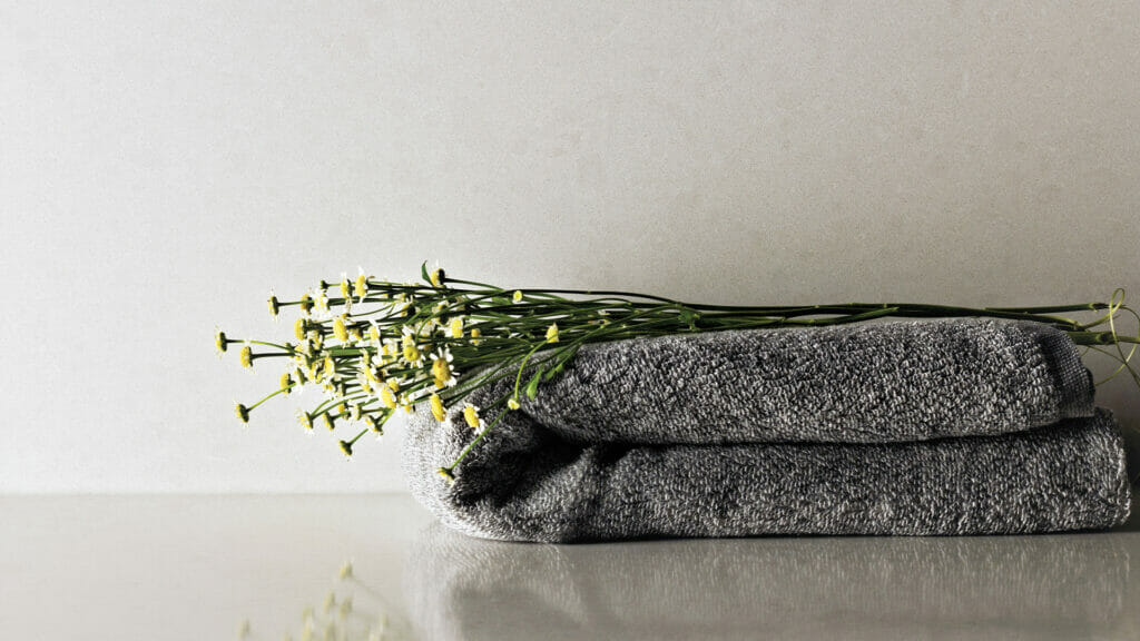 Gray towels stacked neatly with fresh yellow flowers on top, set against a clean and minimalist background.