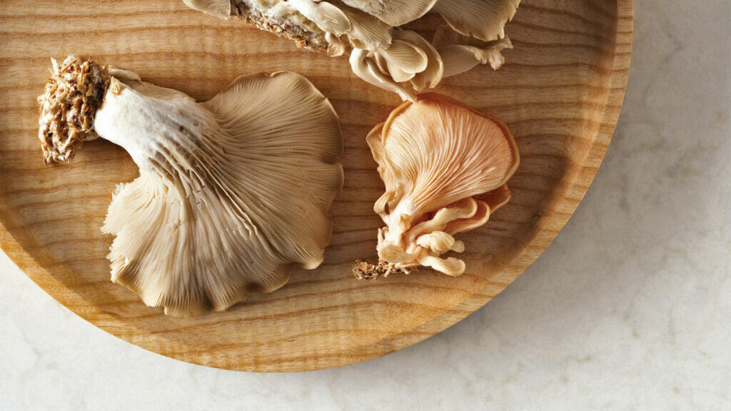 A wooden plate featuring fresh oyster mushrooms in varying shades and textures, showcasing their natural beauty.