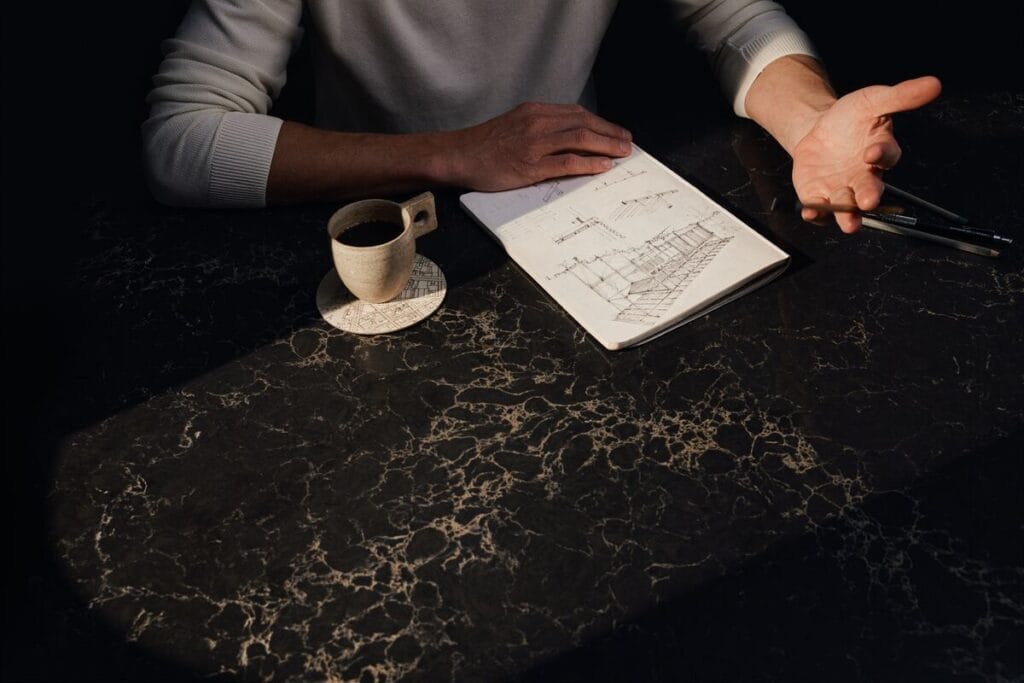 A person's hand gesturing beside a notepad and a coffee cup on a luxurious black marble table.