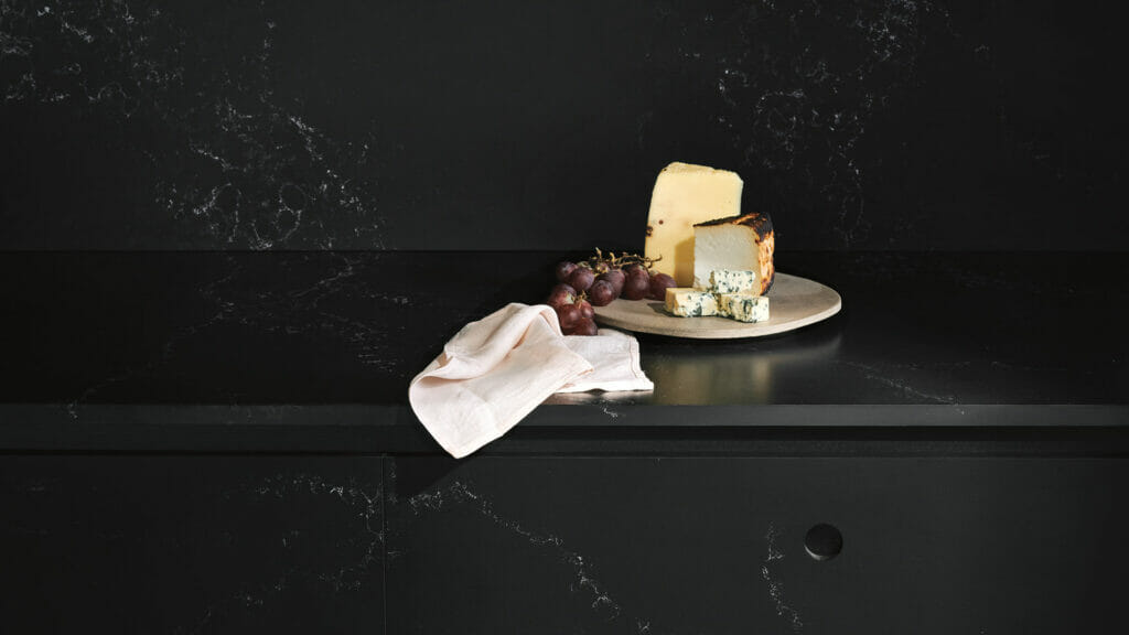 A luxurious black kitchen countertop featuring gourmet cheeses, grapes, and a cloth, highlighting the opulence of Empira Black.
