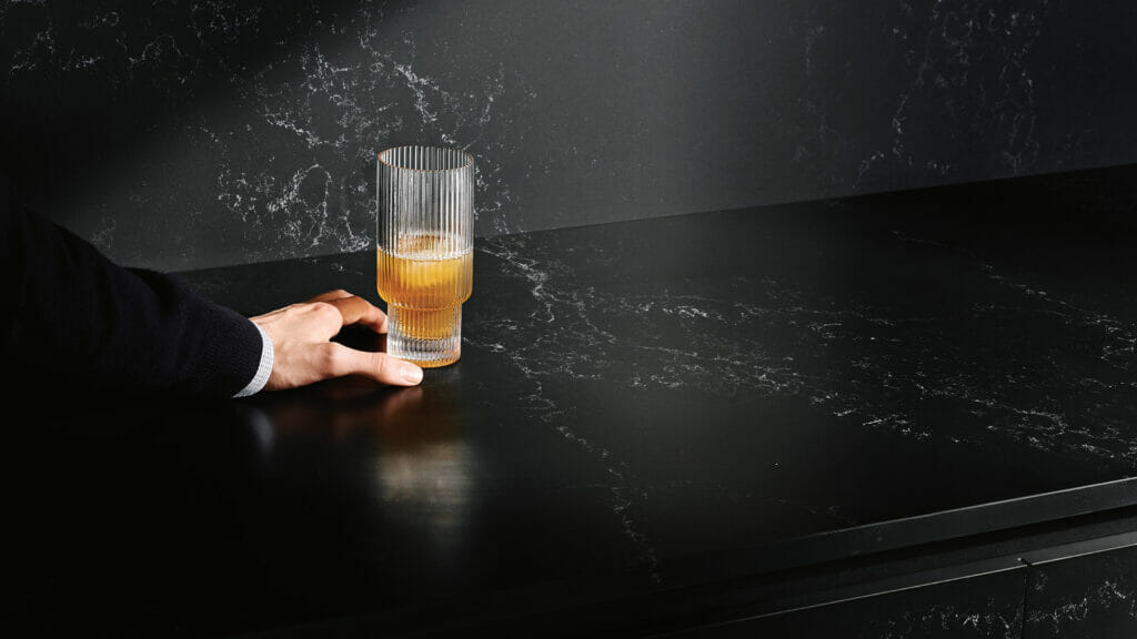 Hand holding a glass on a sleek, dark 5101 Empira Black stone countertop with white veining.