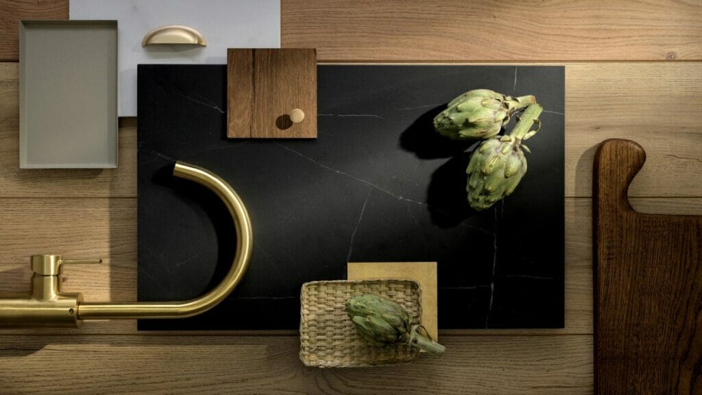 Stylish kitchen countertop featuring dramatic black surface with artichokes, golden faucet, and wooden accents.