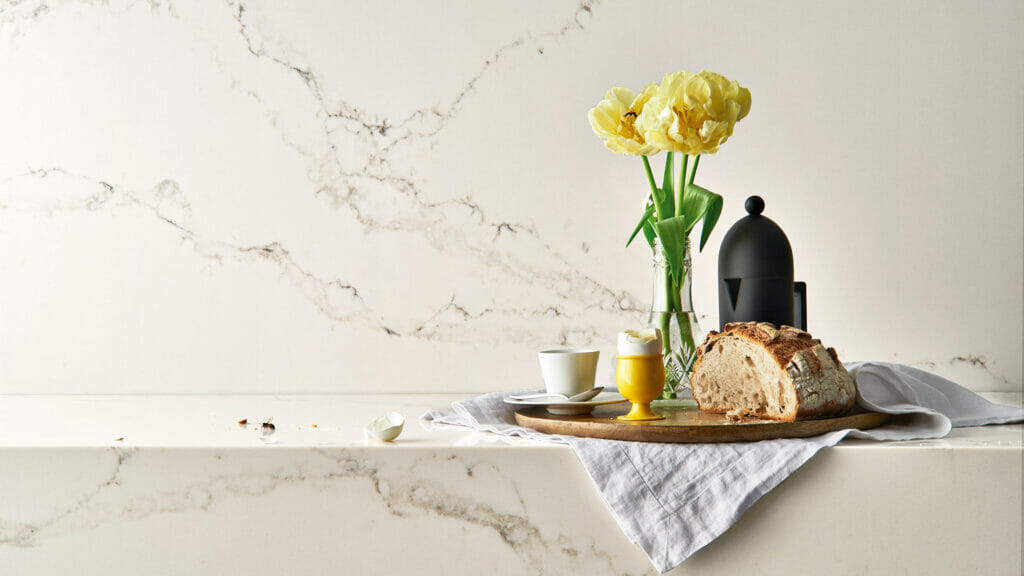 Elegant kitchen scene featuring 5111 Statuario Nuvo countertop with flowers, coffee, and bread, showcasing luxurious marble design.