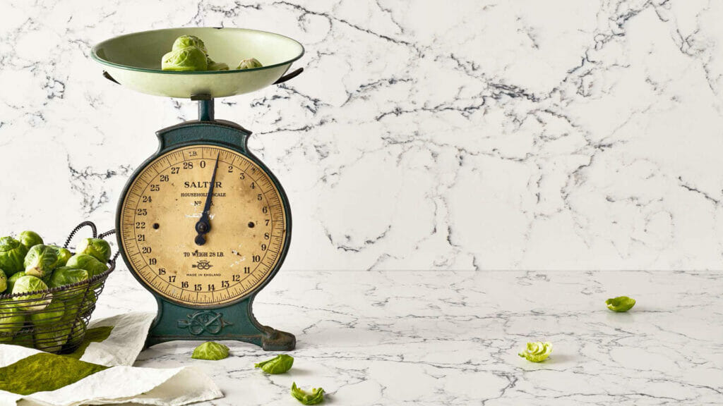 Vintage green scale with brussels sprouts on a marble countertop, showcasing rustic kitchen decor.