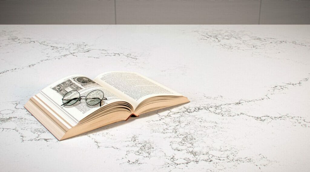 Open book with glasses on a luxurious white countertop featuring subtle shadow patterns.