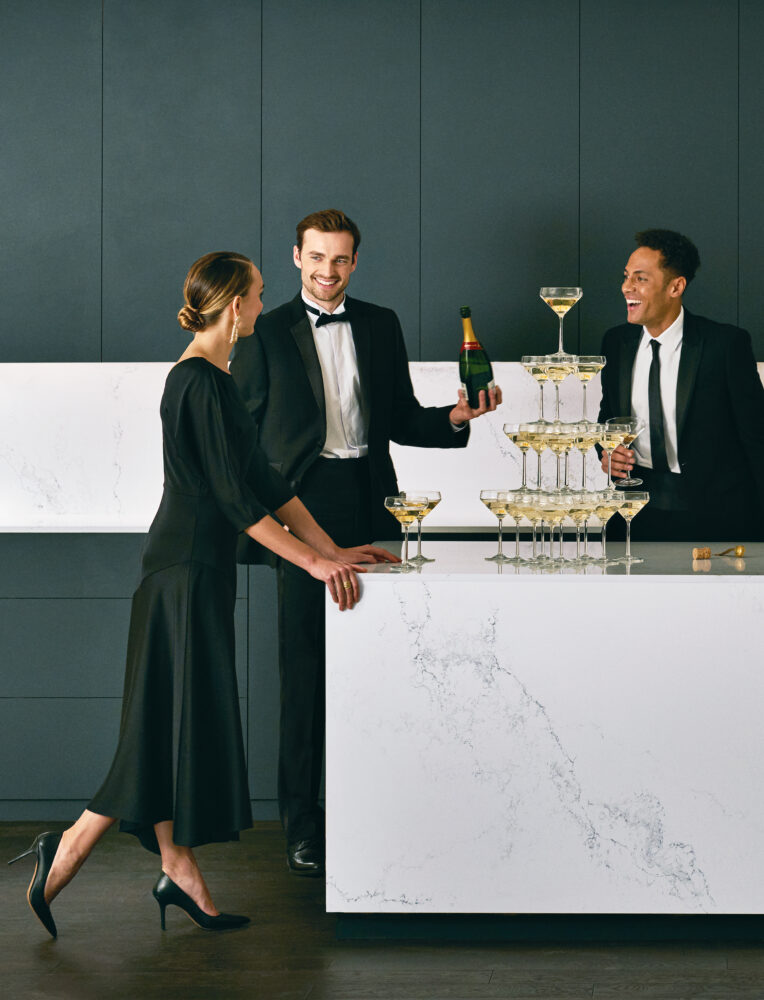 Three elegantly dressed people celebrating with champagne at a marble countertop, showcasing sophistication and style.