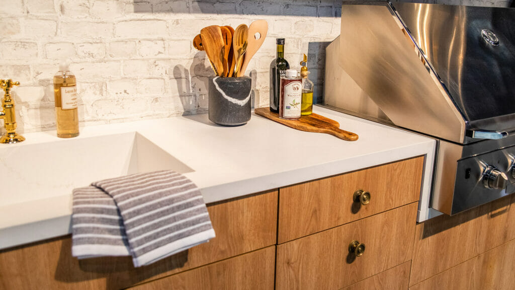Modern kitchen with wooden cabinets, marble countertop, cooking utensils, and grilling area.