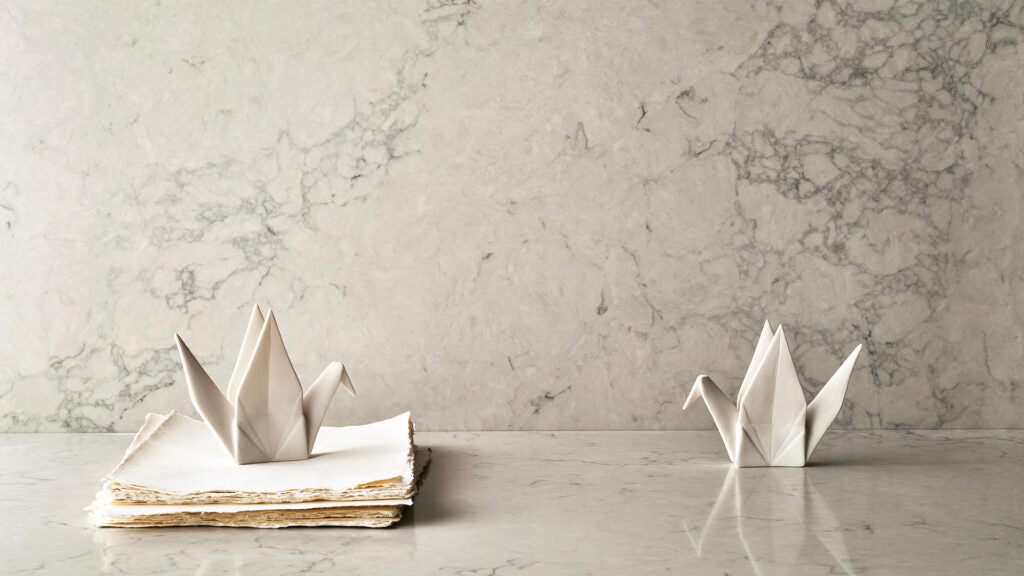 Two white origami cranes on a marble surface, with one on a stack of papers, showcasing intricate paper art.