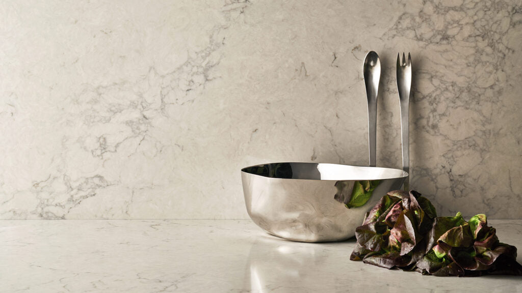 Stylish kitchen scene featuring a shiny bowl, metal utensils, and fresh greens on a marble countertop.
