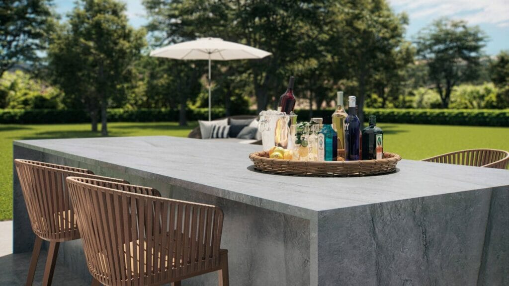 Modern outdoor bar with elephant gray surface, rustic drinks, and stylish wicker chairs in a lush garden setting.