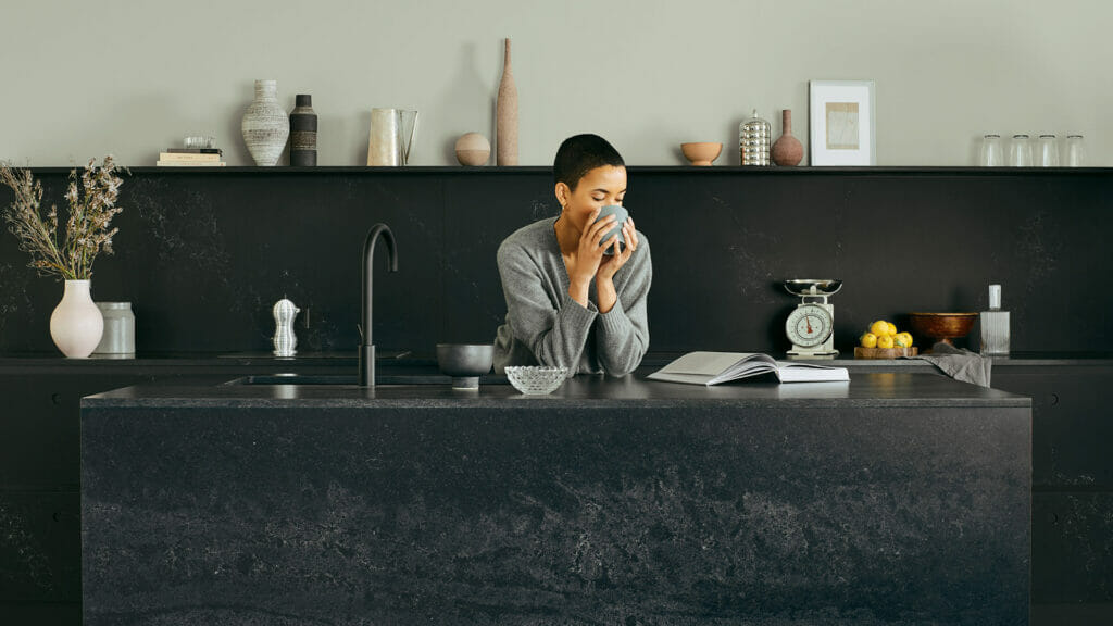 Woman enjoying coffee in a modern black kitchen with a textured countertop and elegant decor.