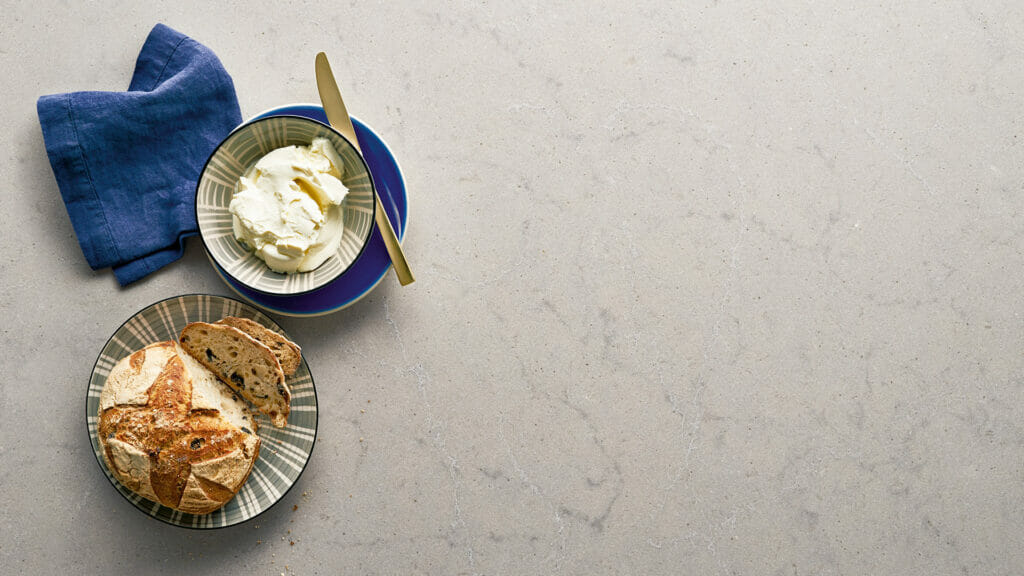 Plate of artisanal bread with a side of creamy cheese and a blue napkin on a light-colored surface.