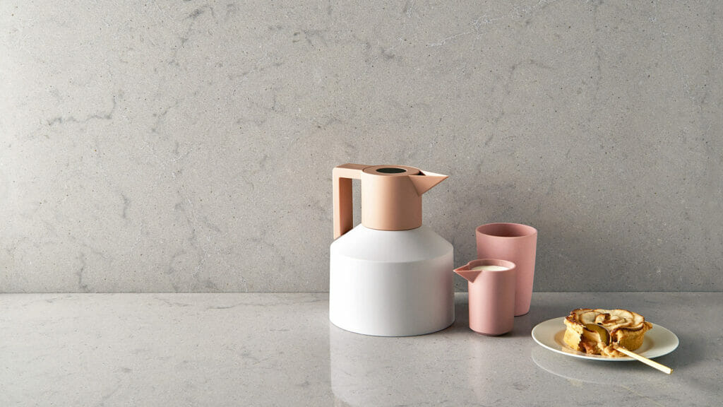 Stylish white and pink kitchen kettle with matching cup alongside a plate of pancakes on a light grey countertop.