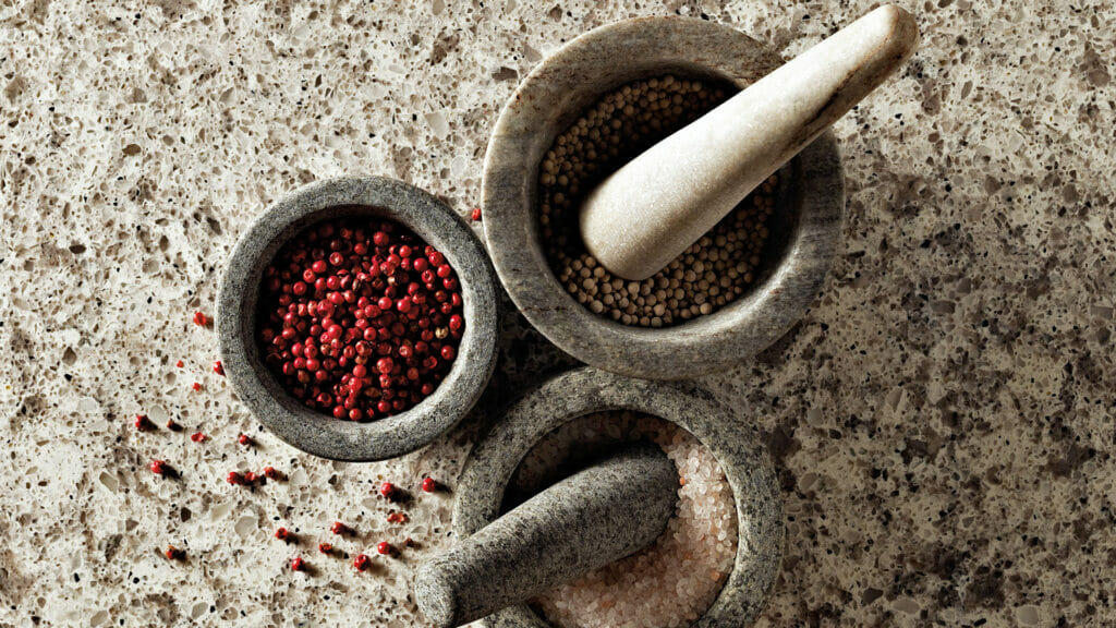 Mortar and pestle with red and black pepper, and unrefined salt on a light grey textured surface.