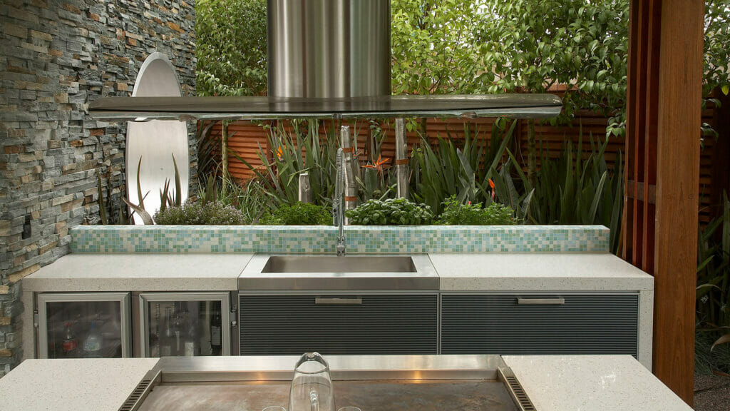 Modern outdoor kitchen featuring sleek cabinetry, a stainless steel sink, and lush greenery for a refreshing ambiance.