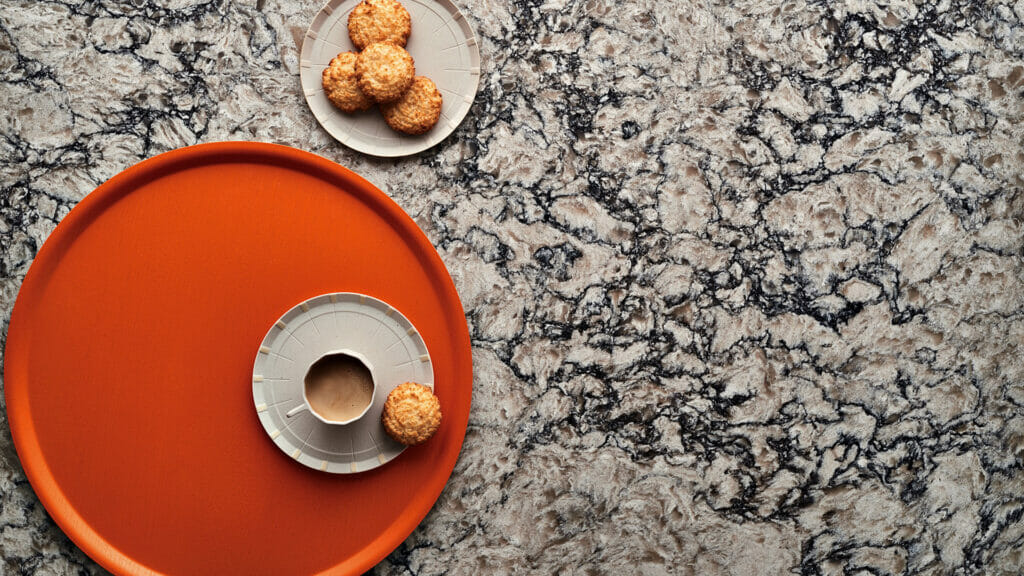 Himalayan Moon granite with dark veining, orange tray, coffee cup, and cookies on a light surface.