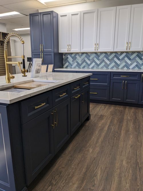 Modern kitchen featuring J&K's navy blue cabinets and white cabinetry with gold hardware and a stylish backsplash.
