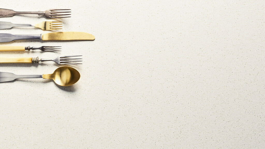 Various elegant utensils including forks, knife, and spoon on a crisp white surface with subtle sparkles.