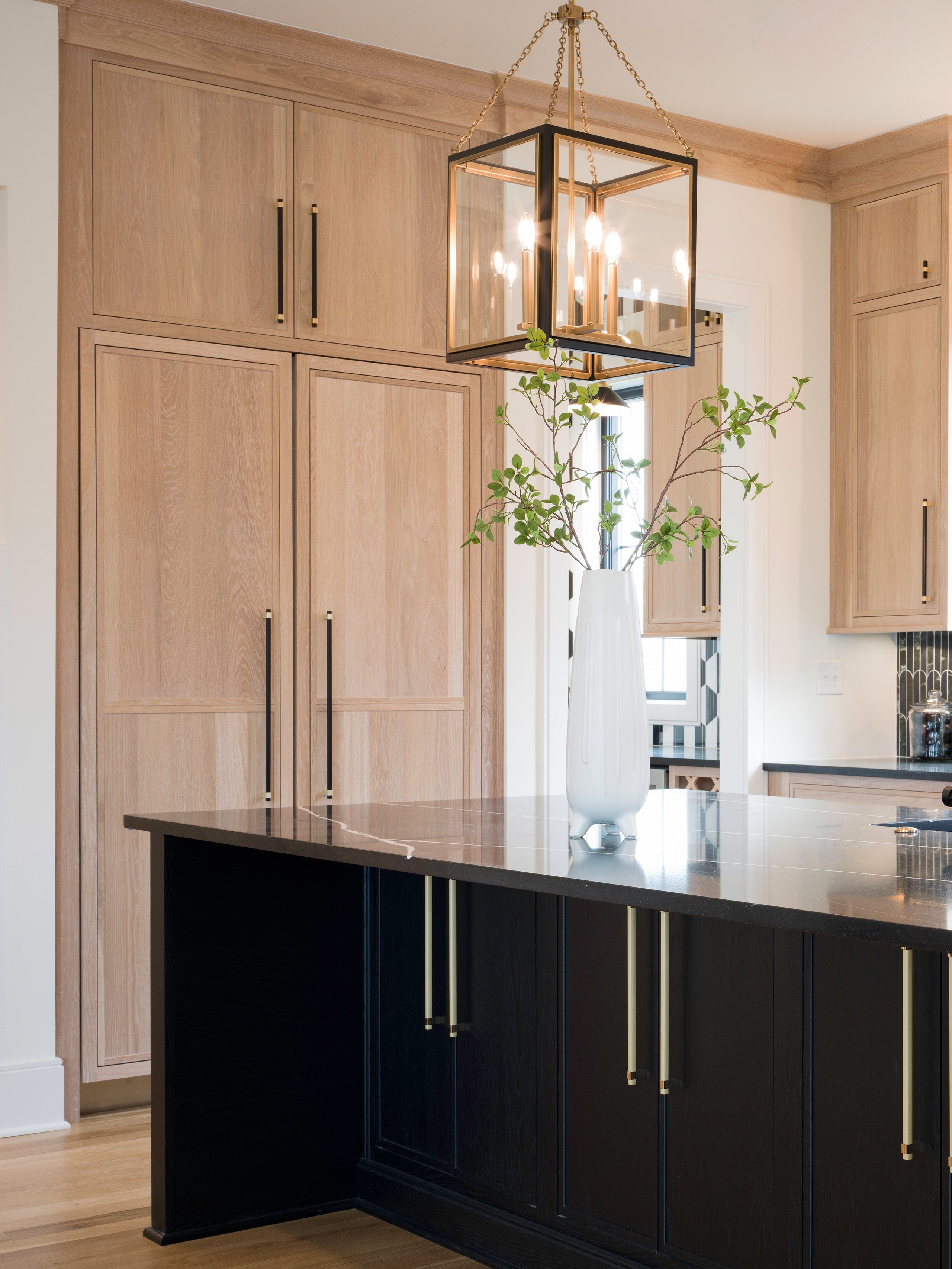 Modern kitchen featuring Shiloh cabinets in light wood and a dark island, complemented by a stylish pendant light.