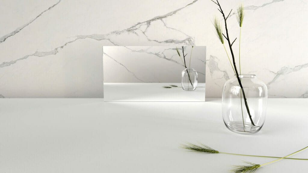Modern minimalist decor featuring a mirror and a glass vase with greenery on a white surface against a marble backdrop.