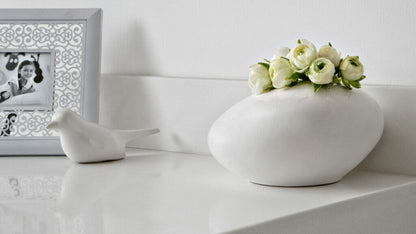 Elegant white decorative vase with fresh flowers on a modern countertop next to a framed photo and a bird figurine.
