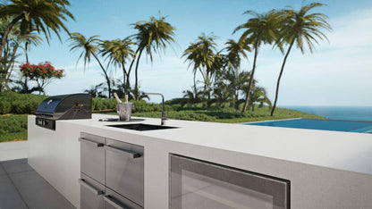 Outdoor kitchen with a modern design, featuring a grill, sink, and a scenic view of palm trees and ocean.