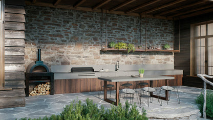 Outdoors kitchen with sleek concrete countertops, rustic stone walls, and wood-fired pizza oven, surrounded by greenery.