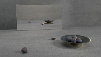 A minimalist setting with a bowl of dark figs and a mirror reflecting the grey concrete ambiance.