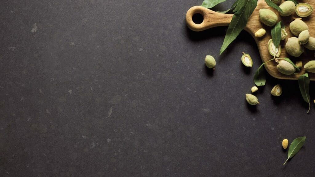 Wooden cutting board with green cardamom pods and leaves on dark slate background.