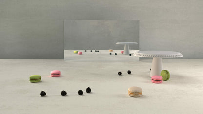 Modern still life with colorful macarons on a light concrete surface and a small white table reflecting in a mirror.