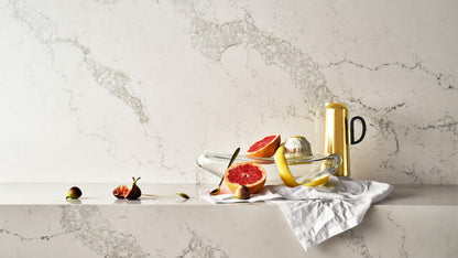 Statuario Maximus countertop displaying fresh fruits and a golden pitcher, showcasing elegant dove-white with grey veining.