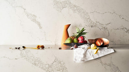 Statuario Maximus countertop with fruits, vase, and copper bowls on a clouded grey veined surface.