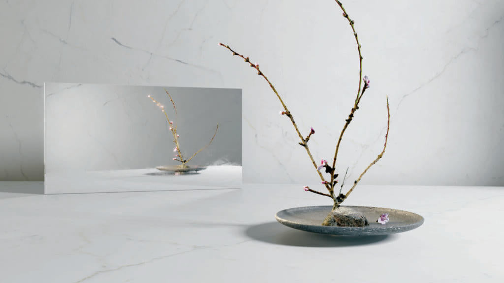 Elegant arrangement of delicate branches with blossoms on a textured plate against a marble backdrop.