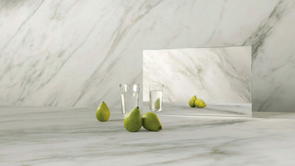 Elegant display of 505 Archetta marble with grey veins, green pears, and glass reflections on a soft ivory-white surface.