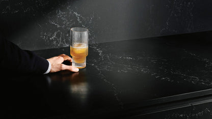 Hand holding a glass on a sleek, dark 5101 Empira Black stone countertop with white veining.