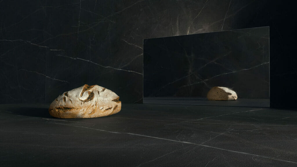 Honed black surface with a loaf of bread and a reflective mirror, showcasing dramatic contrasts in texture.