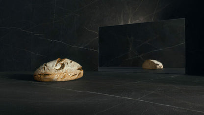 Honed black surface with a loaf of bread and a reflective mirror, showcasing dramatic contrasts in texture.