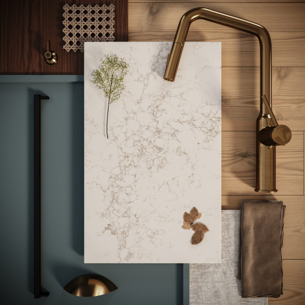 Creamy white countertop with organic grey veining, featuring a leaf decoration and a stylish gold faucet.
