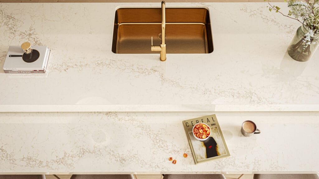 Modern kitchen countertop featuring creamy white surface with grey veining, gold faucet, and stylish decor.