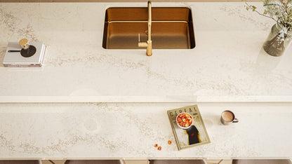 Modern kitchen countertop featuring creamy white surface with grey veining, gold faucet, and stylish decor.