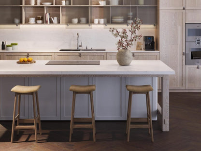 Modern kitchen featuring a sleek white island, wooden stools, and decorative vase with flowers.