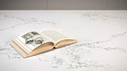 Open book with glasses on a luxurious white countertop featuring subtle shadow patterns.