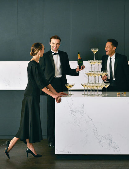 Three elegantly dressed people celebrating with champagne at a marble countertop, showcasing sophistication and style.